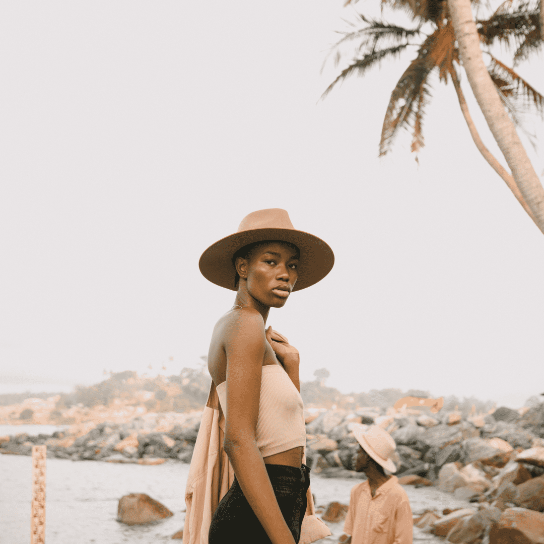 A woman standing on a rocky shore wearing a wide brim wool hat