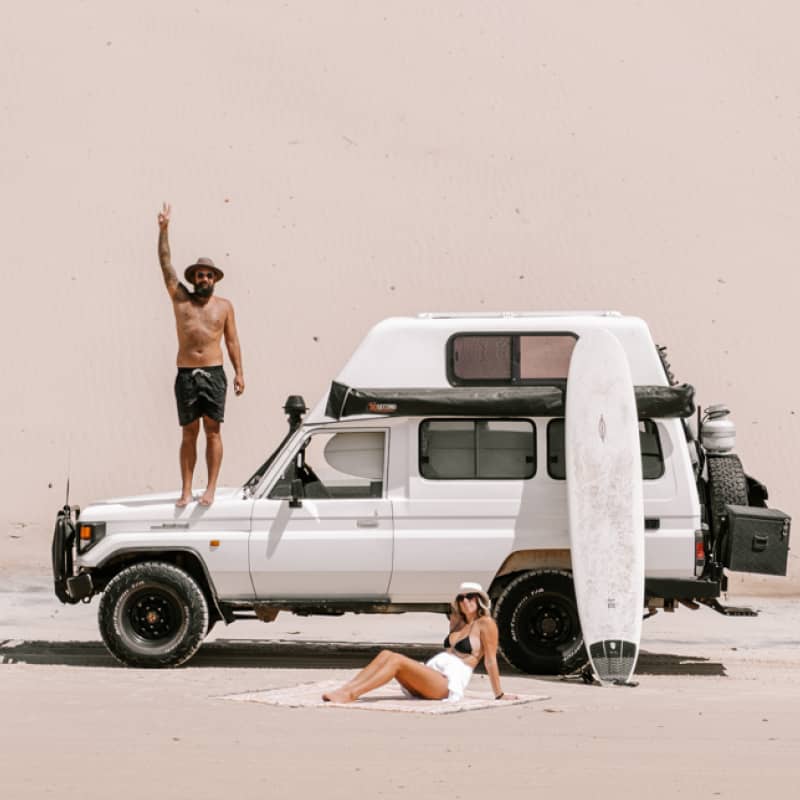 A couple next to their parked 4WD camper on the beach