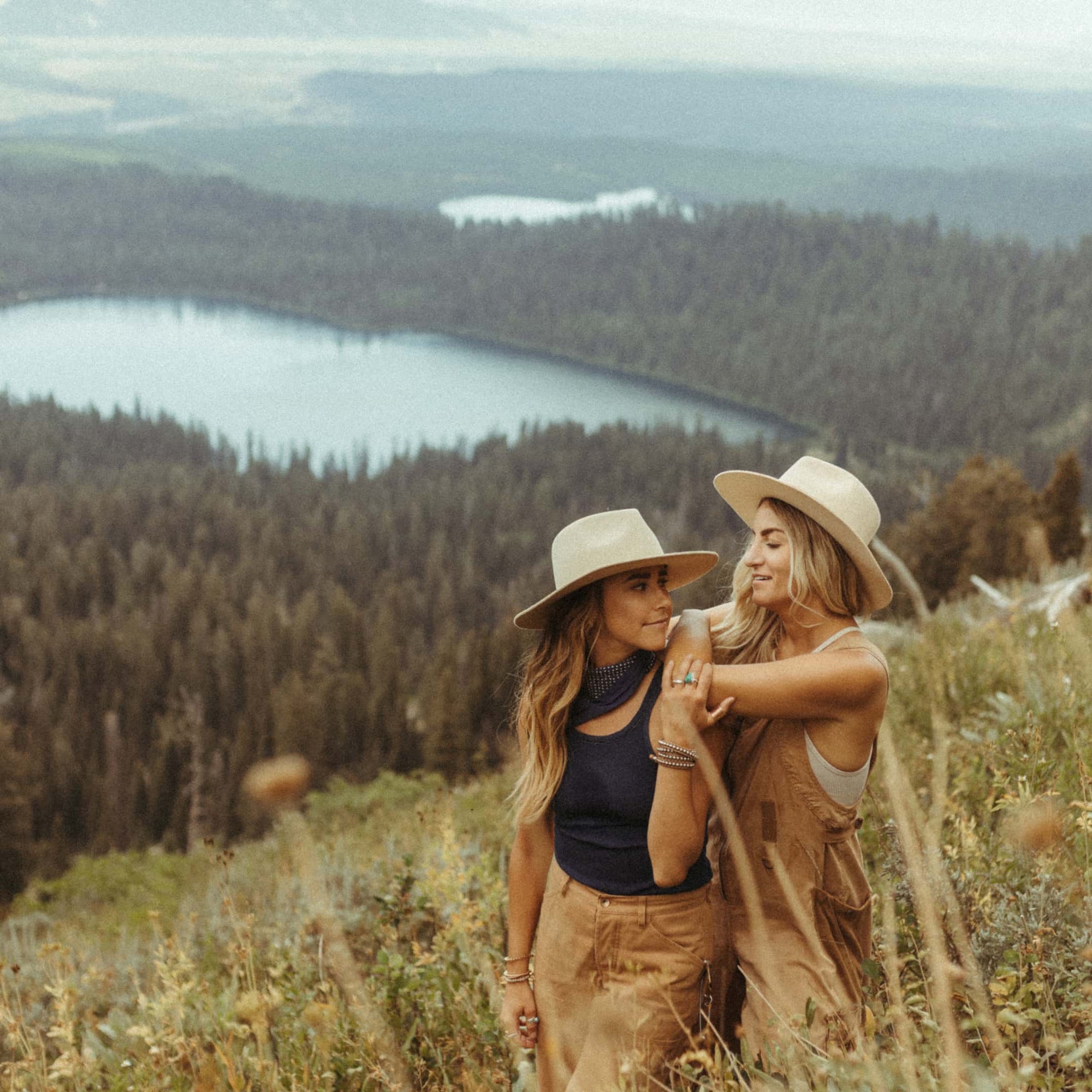 Taryn standing with her arms over Amanda while they stand in a grassy field on top of a mountain