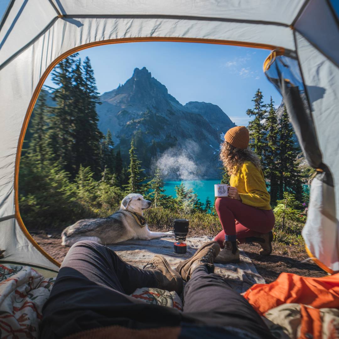 Chelsea and her dog sitting outside their tent entrance looking towards the mountains in the distance