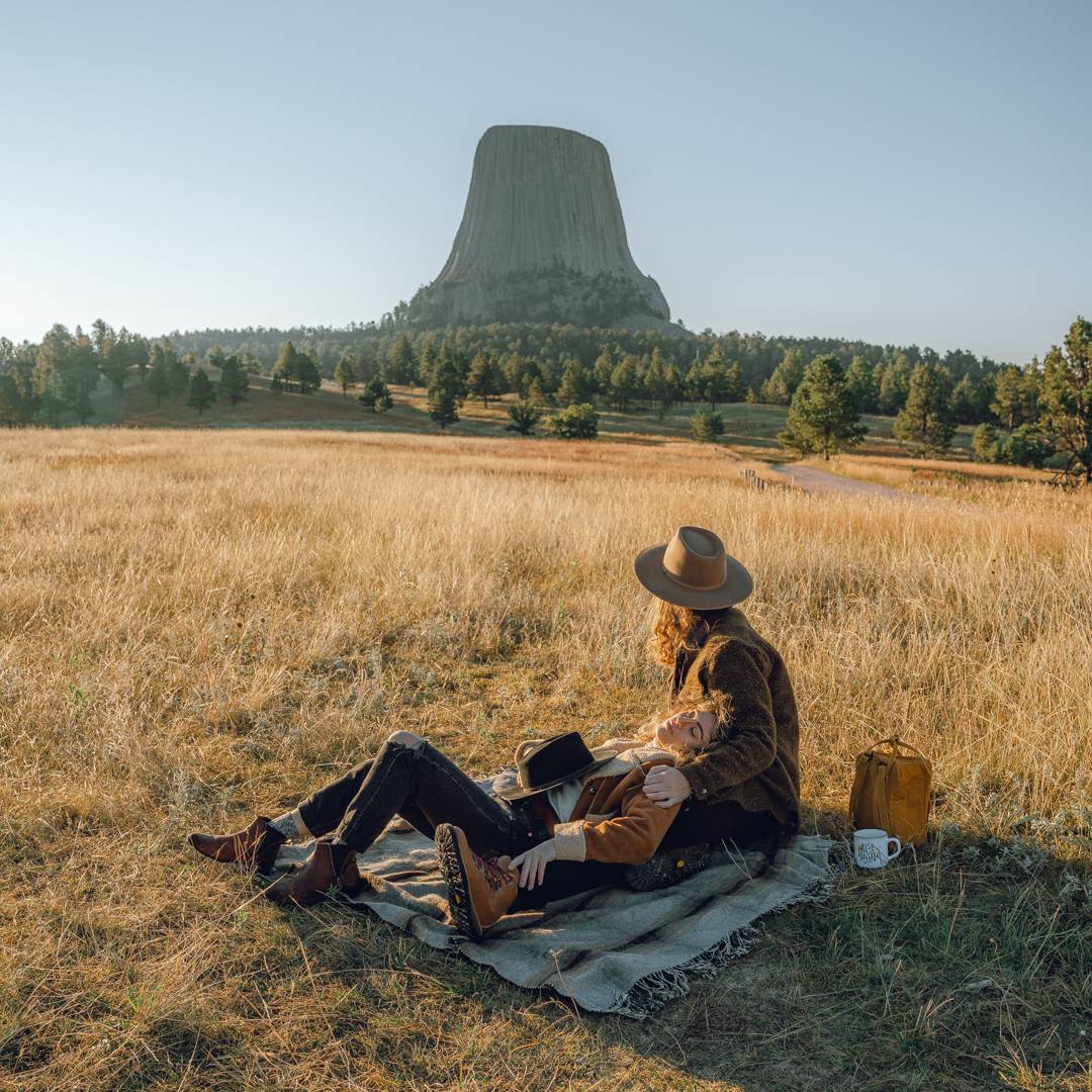 Brayden and Chelsea sit on a picnic blanket looking out towards Devils Tower in Wyoming