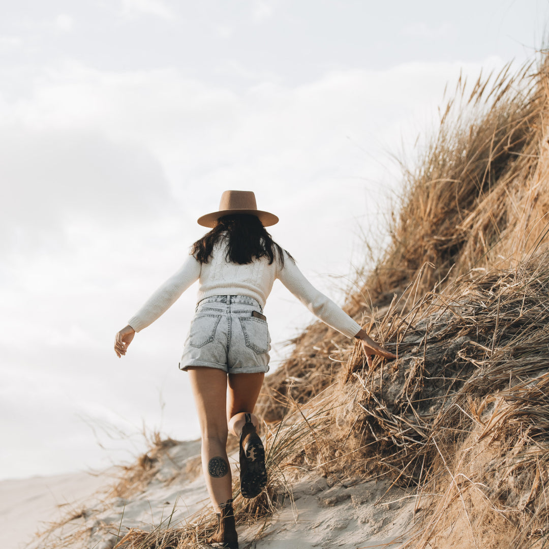 A woman wearing a wide brim hat is running up a sand dune