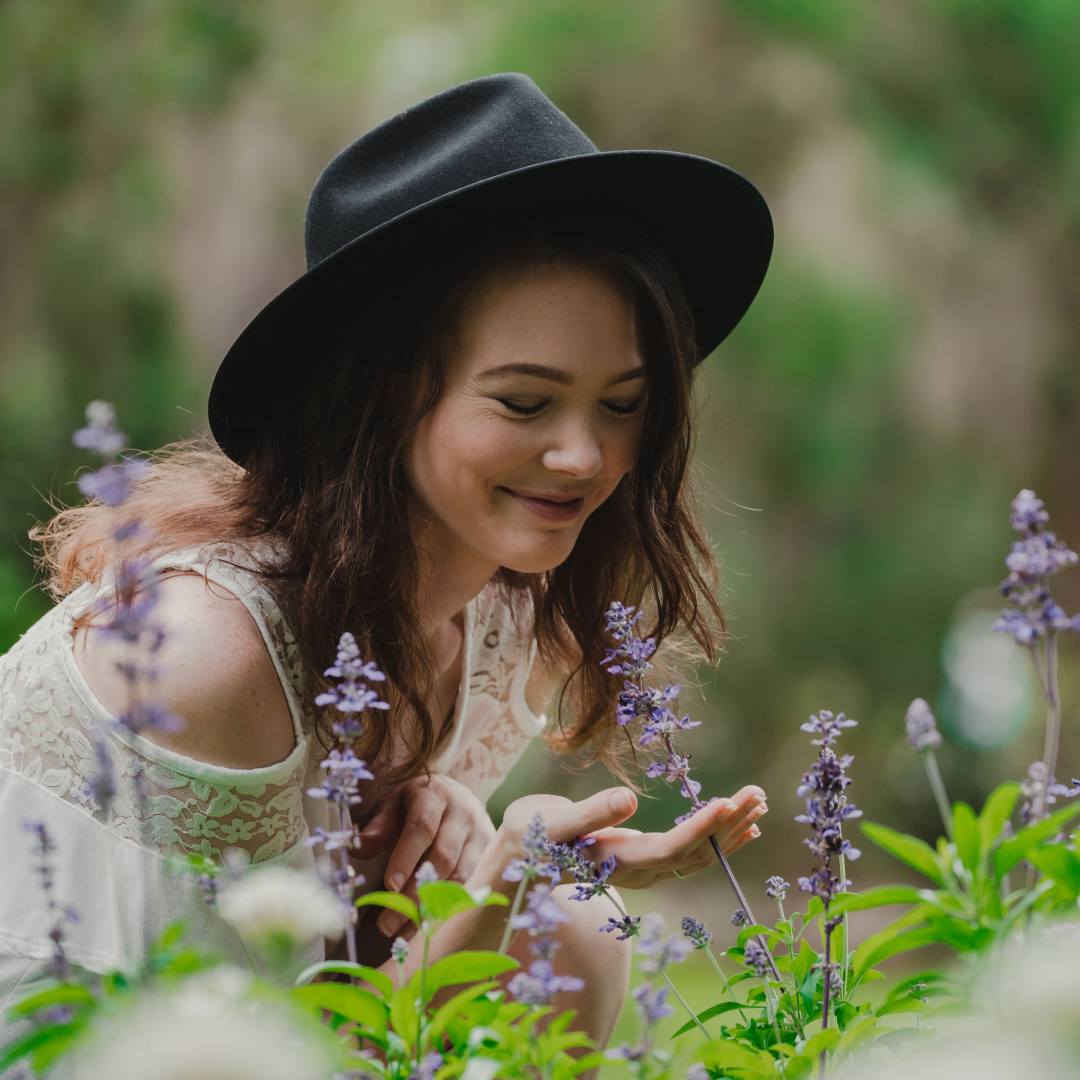 Young woman wearing a hat smelling flowers in a garden