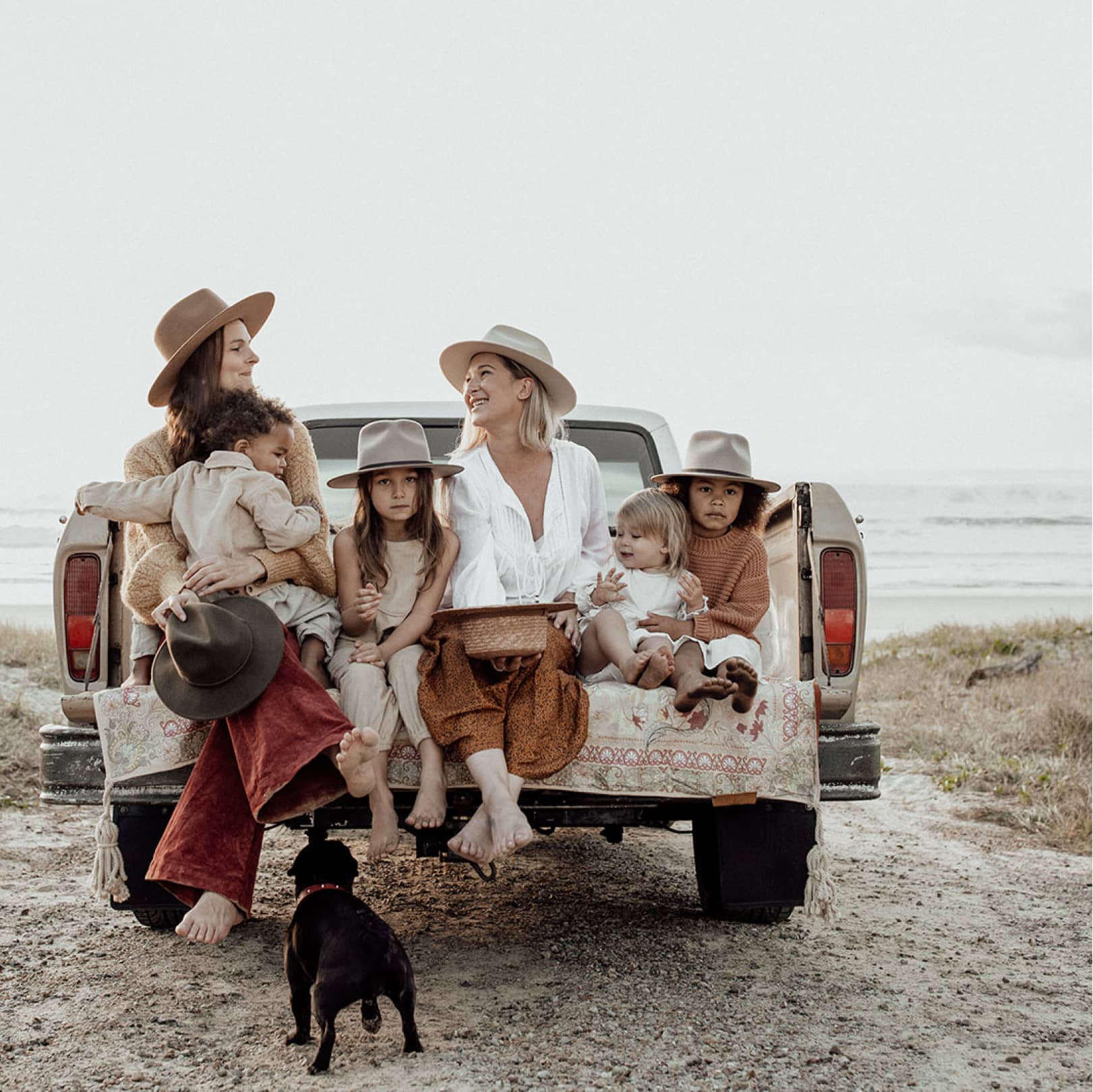 Two women sitting together in the back of a ute tray with their children next to them