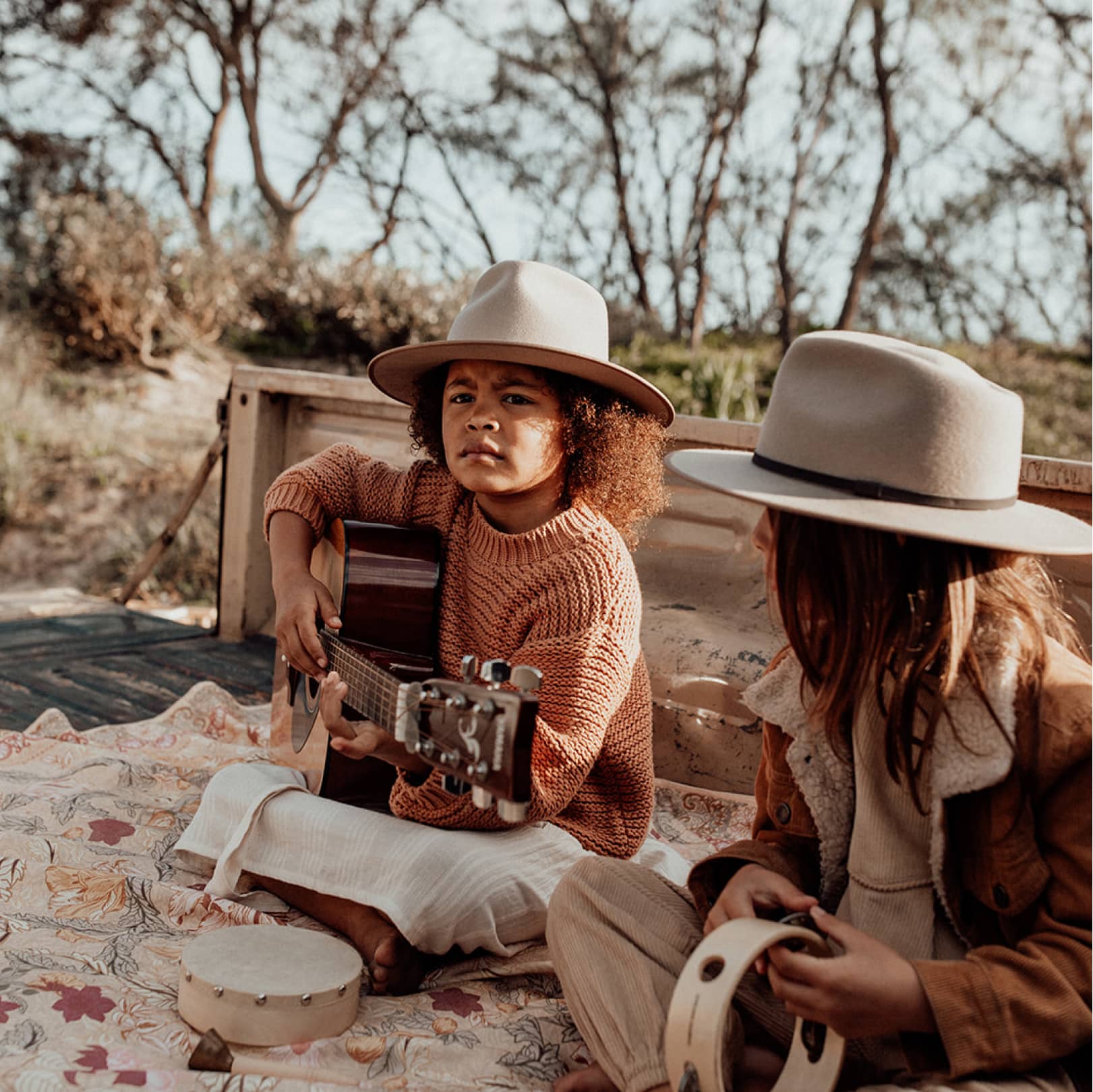 Two children sitting on a picnic rug playing the guitar and tamborine