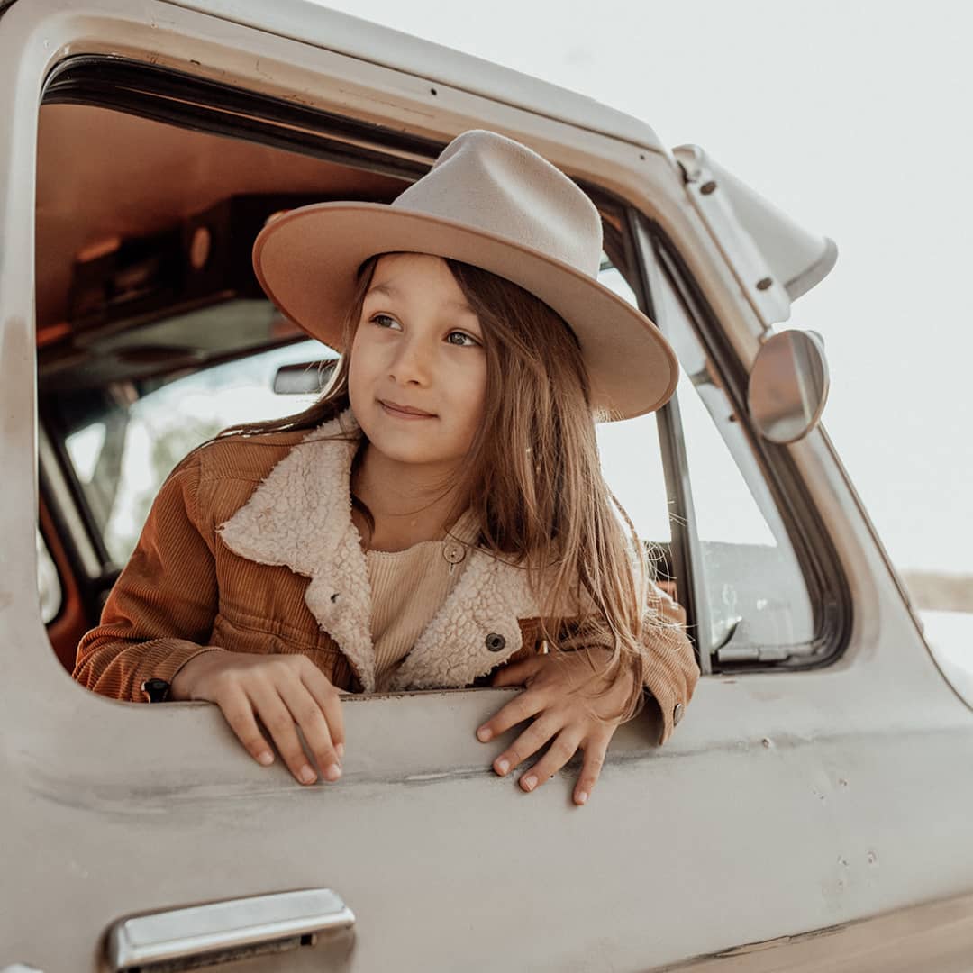 Child in a wide brim wool hat sitting inside a car and looking out the window