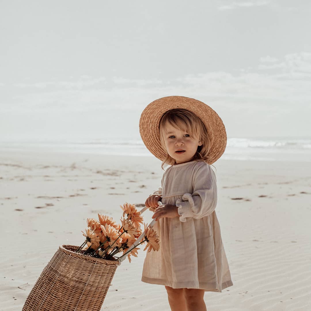 Toddler pushing a wicker basket full of flowers along the beach