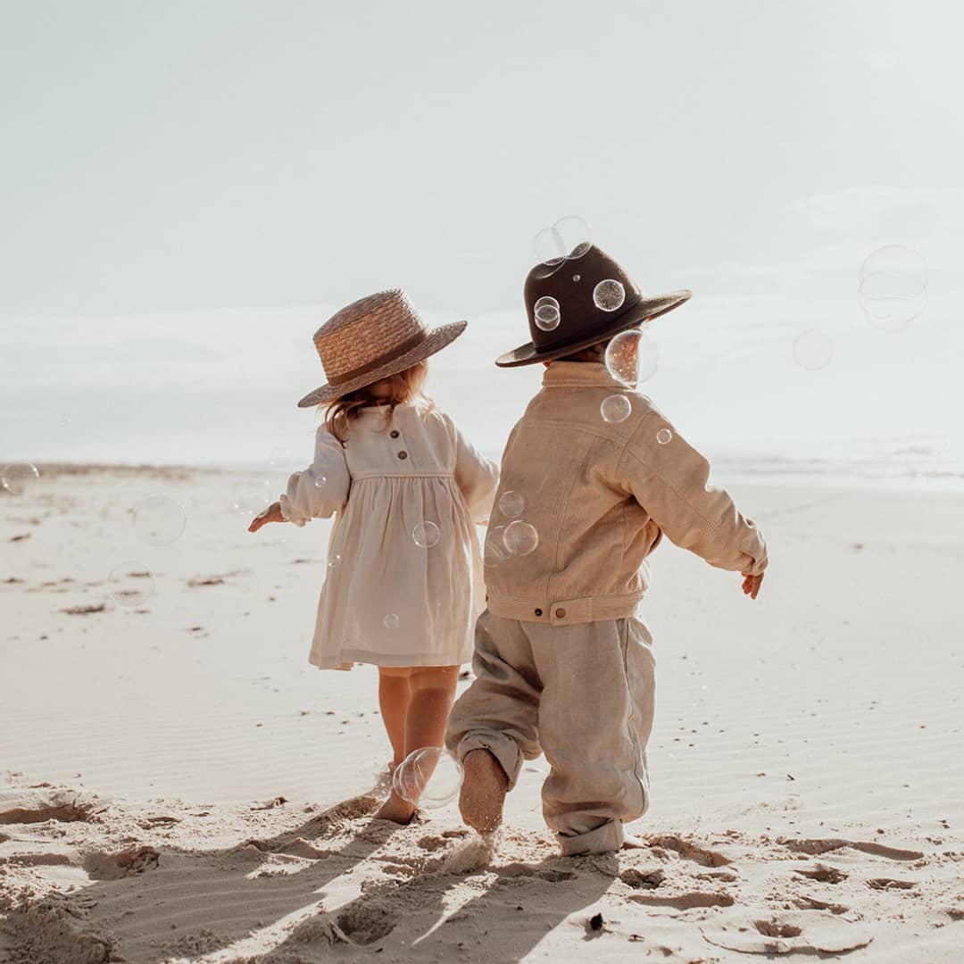 Two children running through bubbles on the beach