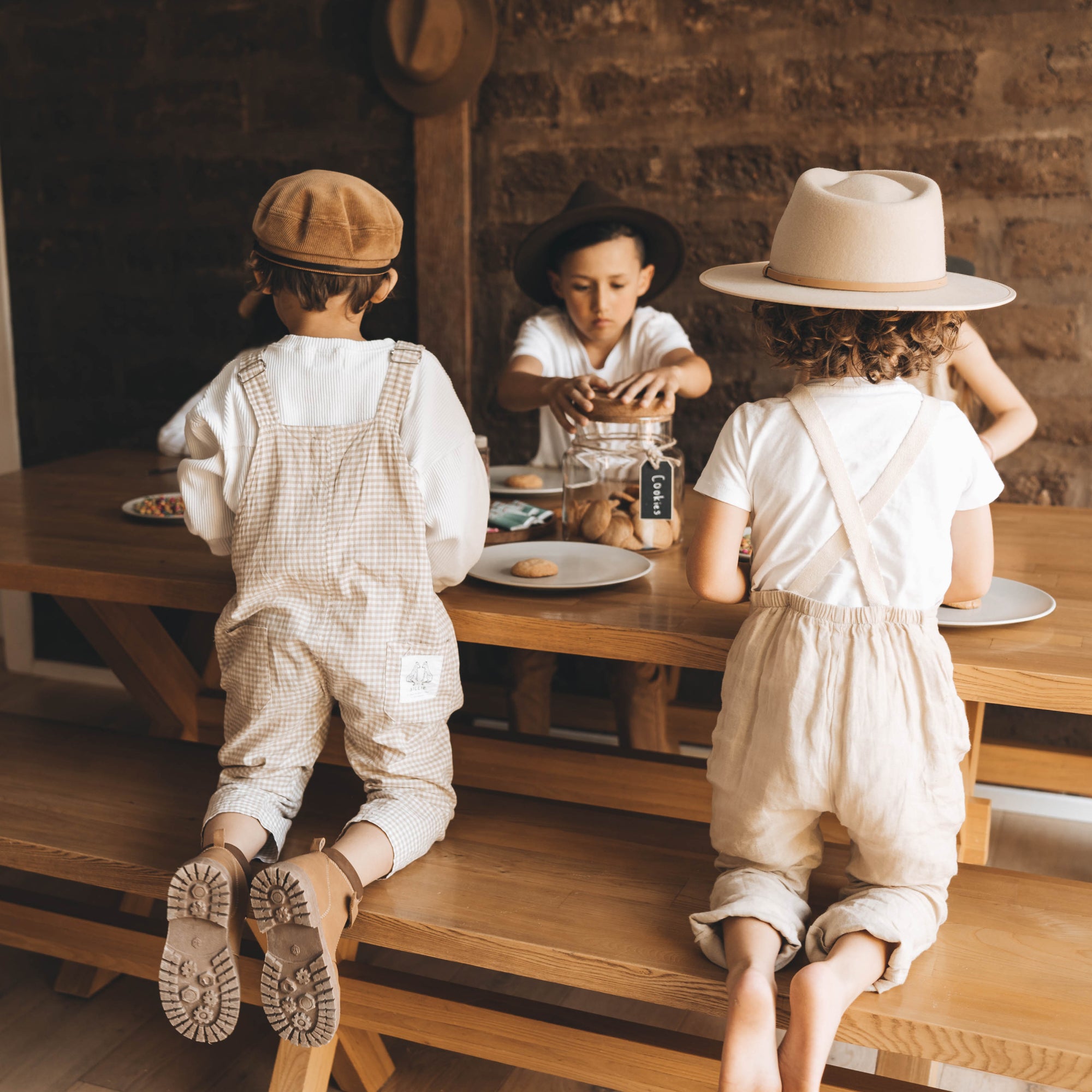 A group of young children are sitting around a wooden table icing cookies