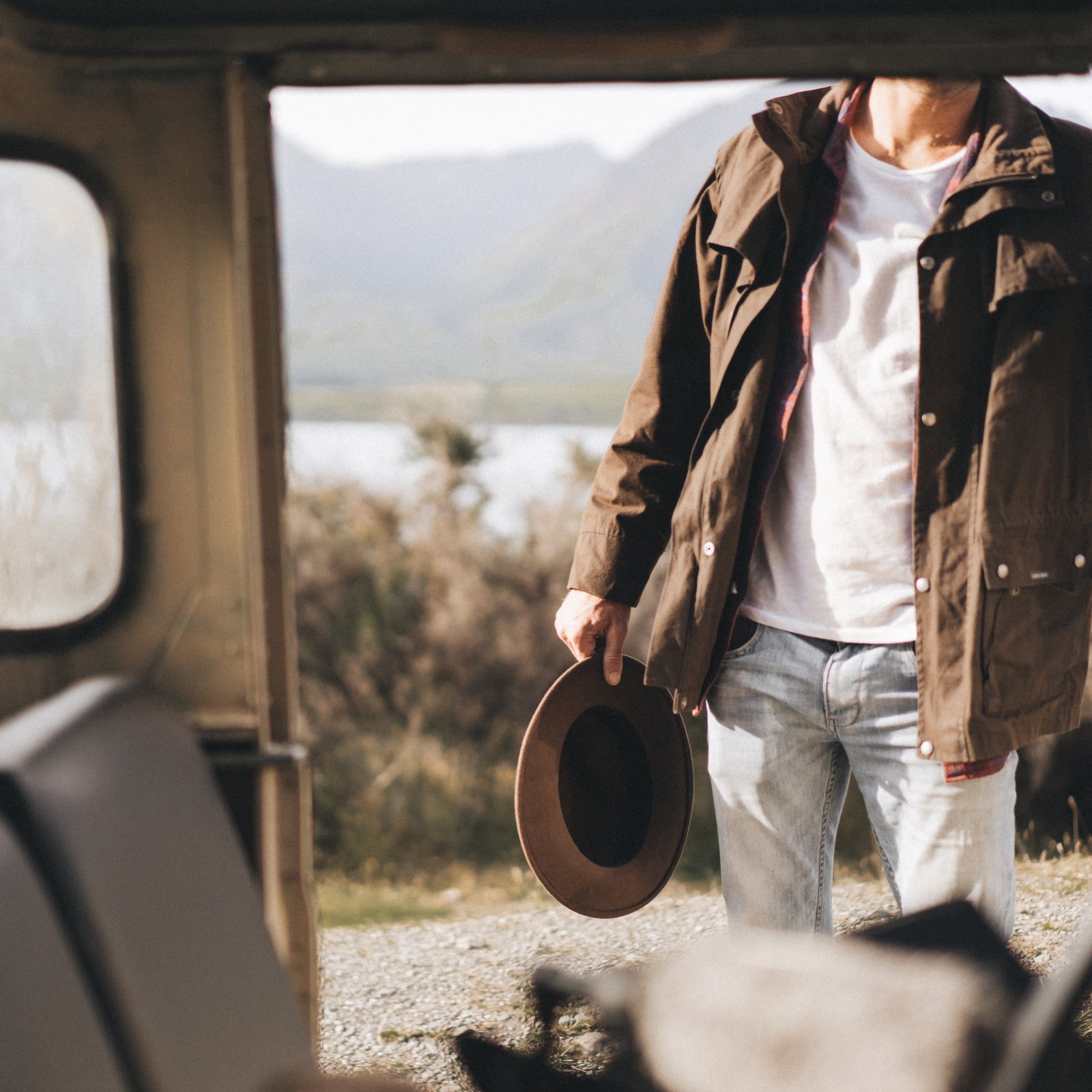 A close up photo of a persons hand, standing outside a car holding a wide brim wool hat