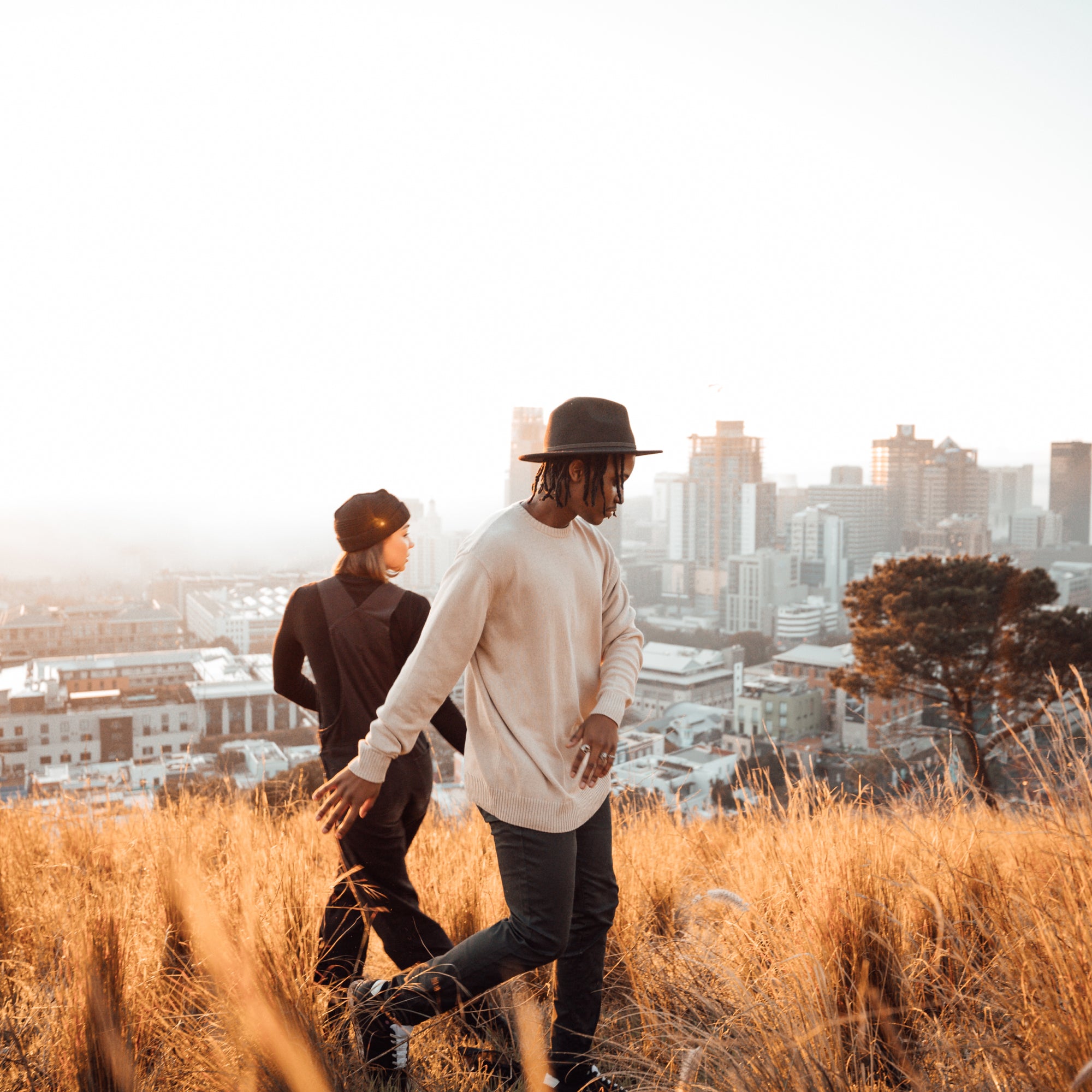 A woman and a man running through a long grassy field with the cityscape behind them in Cape Town