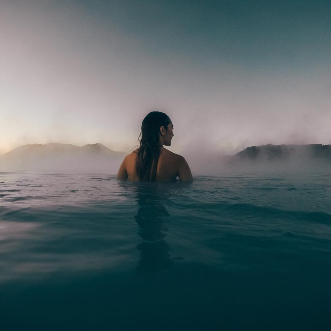 A woman in the middle of the water looking ahead to some fog and mountains in the distance