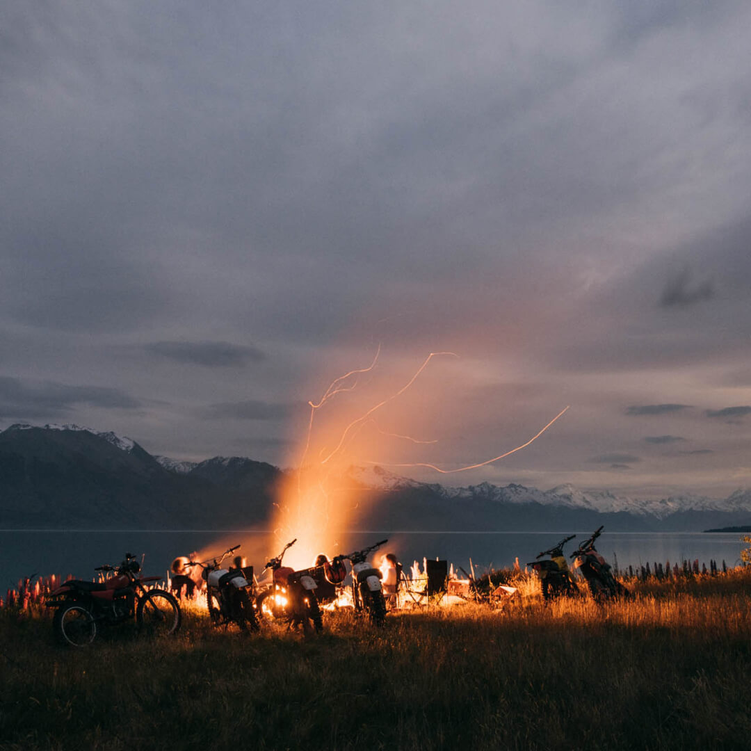 A bunch of motorbikes parked around a camp fire at night