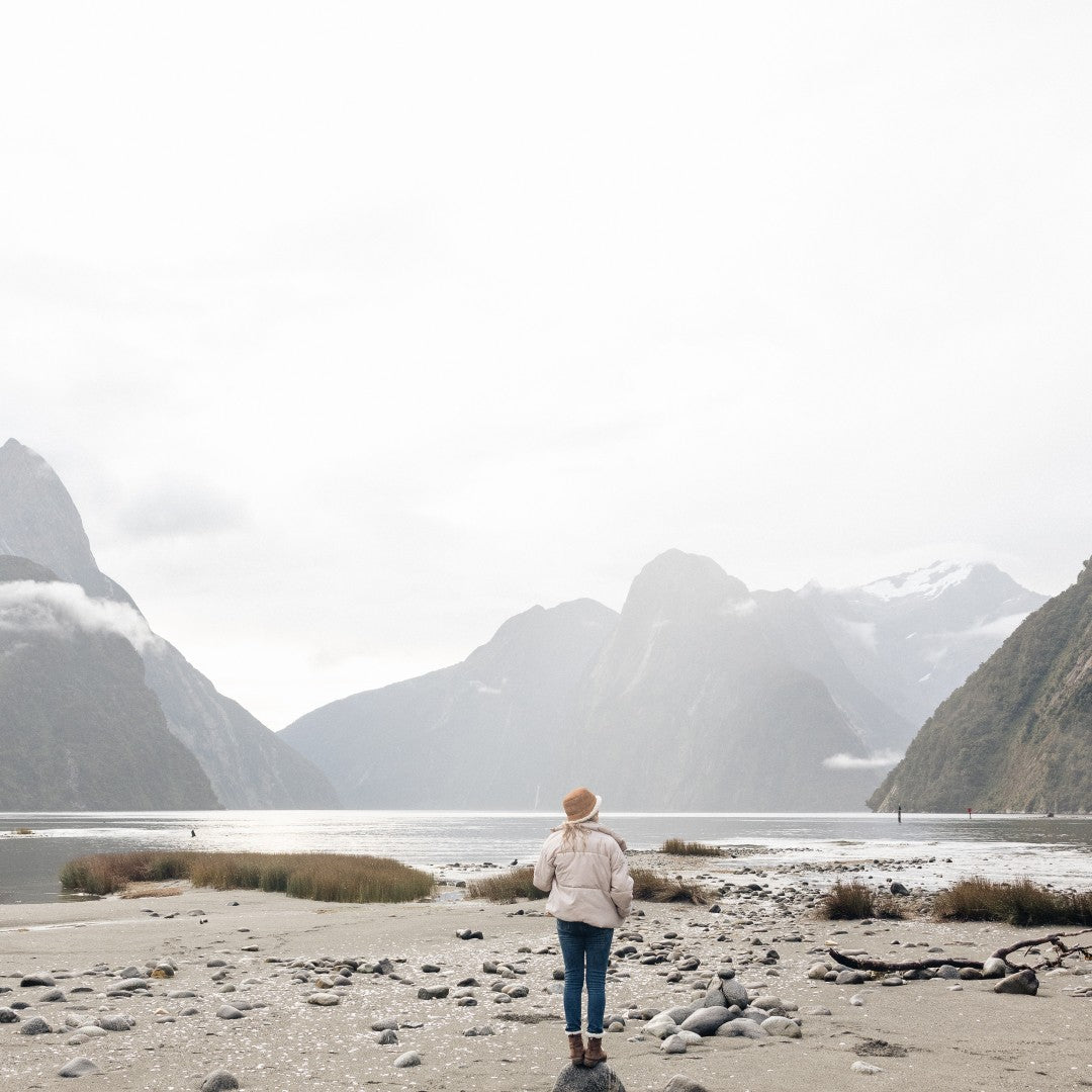 woman standing on a rock at the beach wearing a bucket hat