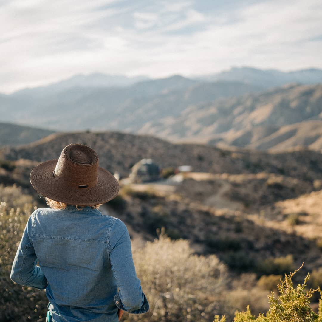 A woman wearing a large straw hat looking out over mountain valley views