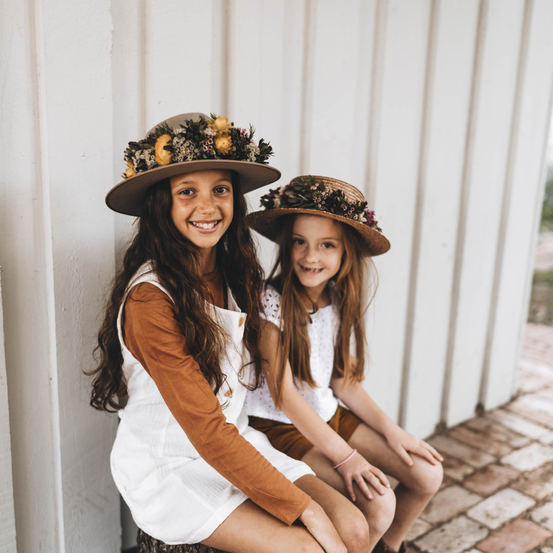Two young girls wearing wide brim wool hats with flowers around the crown
