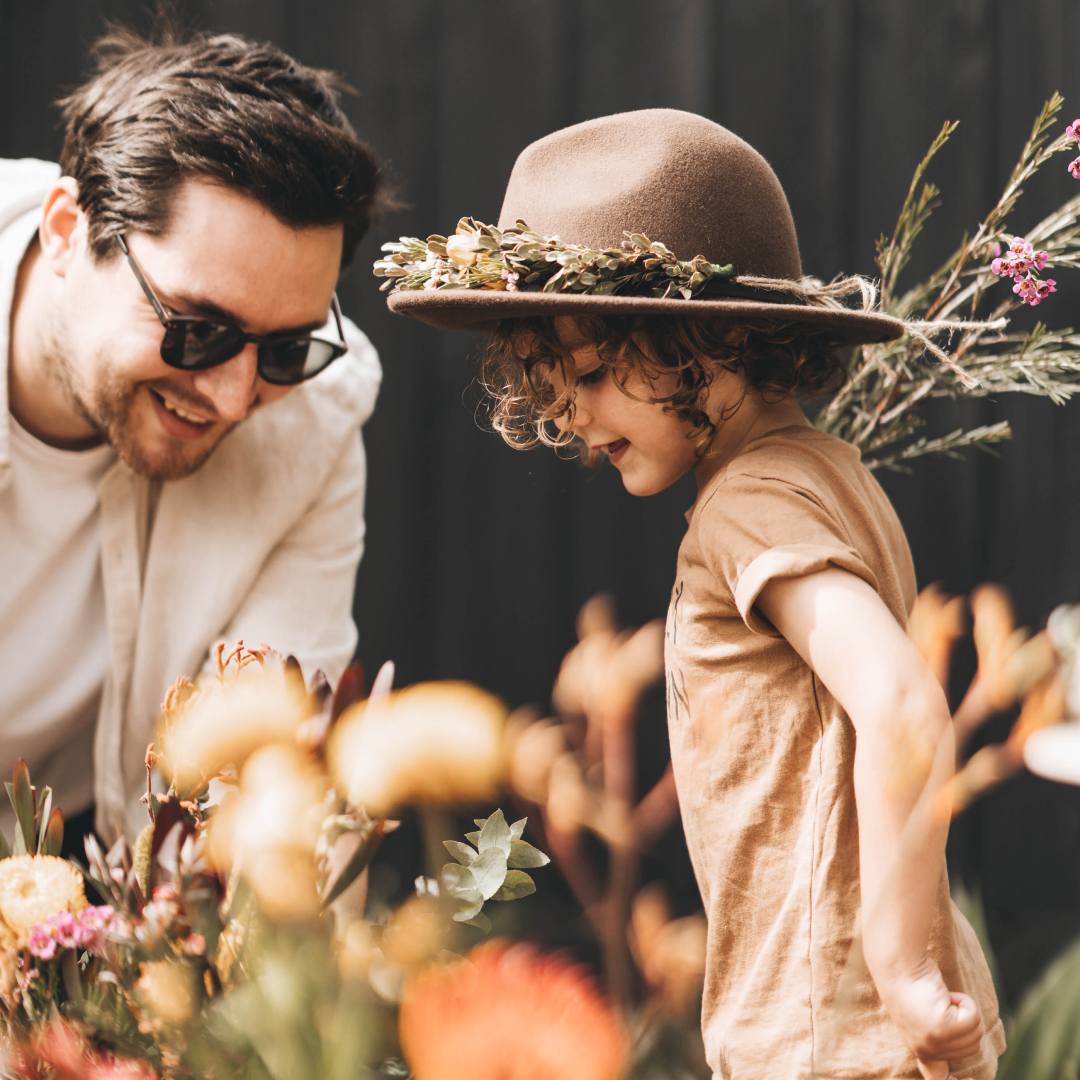 A father and his young son are arranging flowers to put on wide brim wool hats
