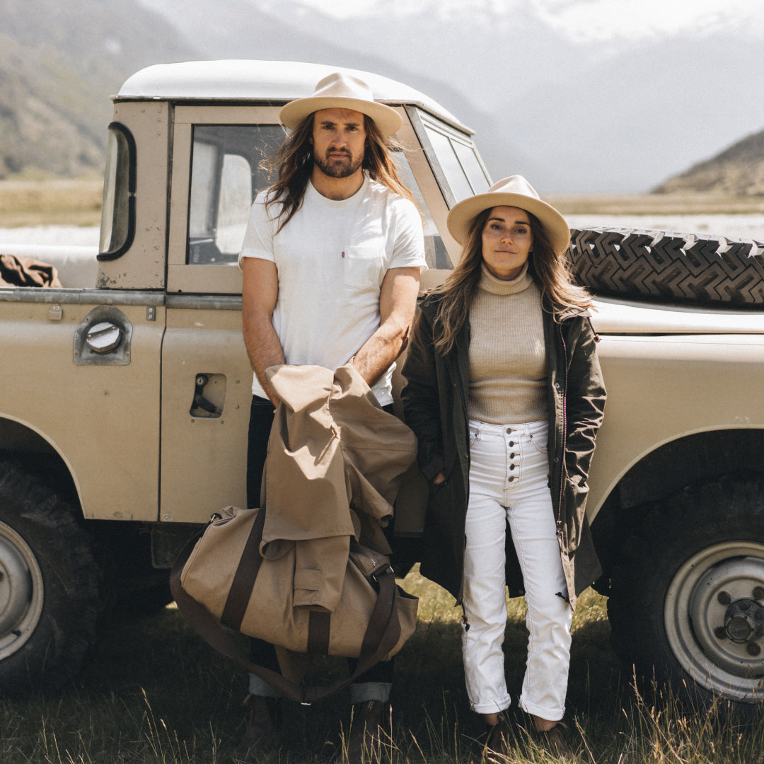 Alex and Loz holding their Driza-Bone jackets, leaning against the side of a 4WD