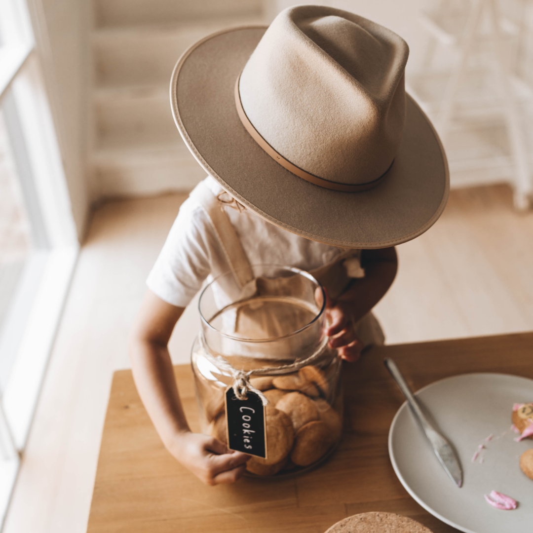 A young boy wearing a wide brim wool hat is holding a cookie jar