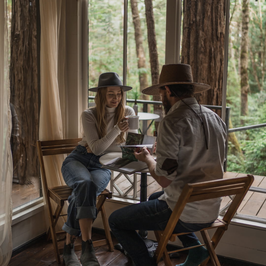 A man and a woman sitting at a table looking at books in a tree house cabin