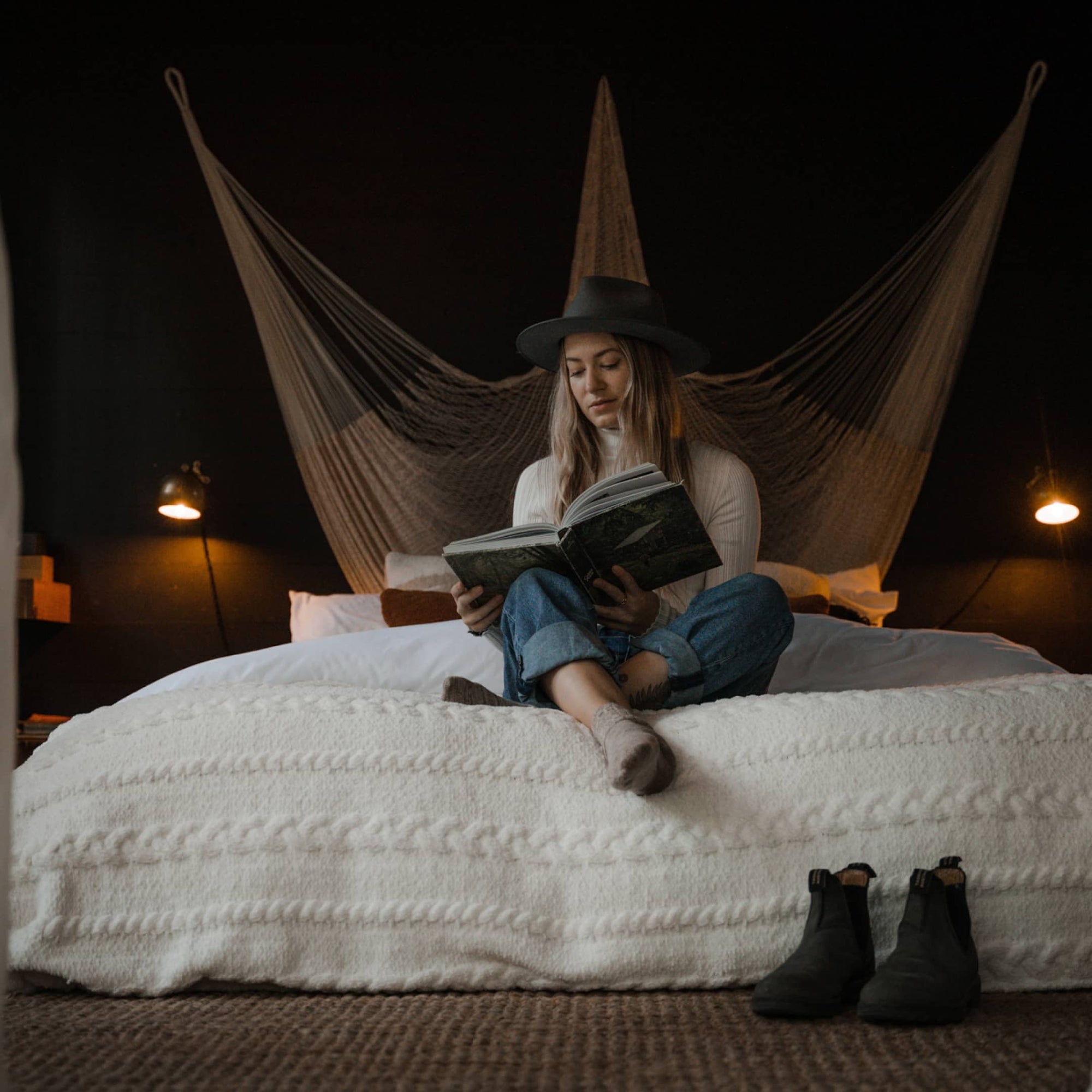 Melissa sitting inside a cabin on top of a large bed reading a book