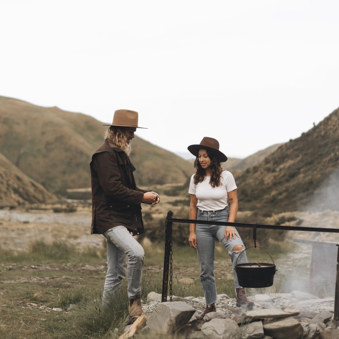 A man and a woman in a mountain valley cooking food over a camp fire