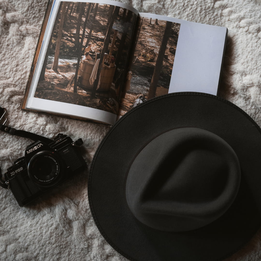 Close up photo of a book, film camera and a wide brim wool hat