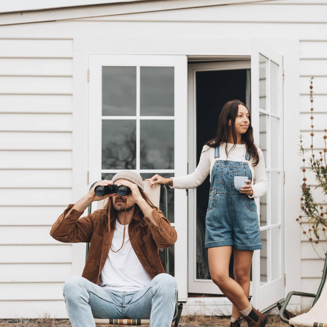 A man and a woman out the front of a cottage looking at the view