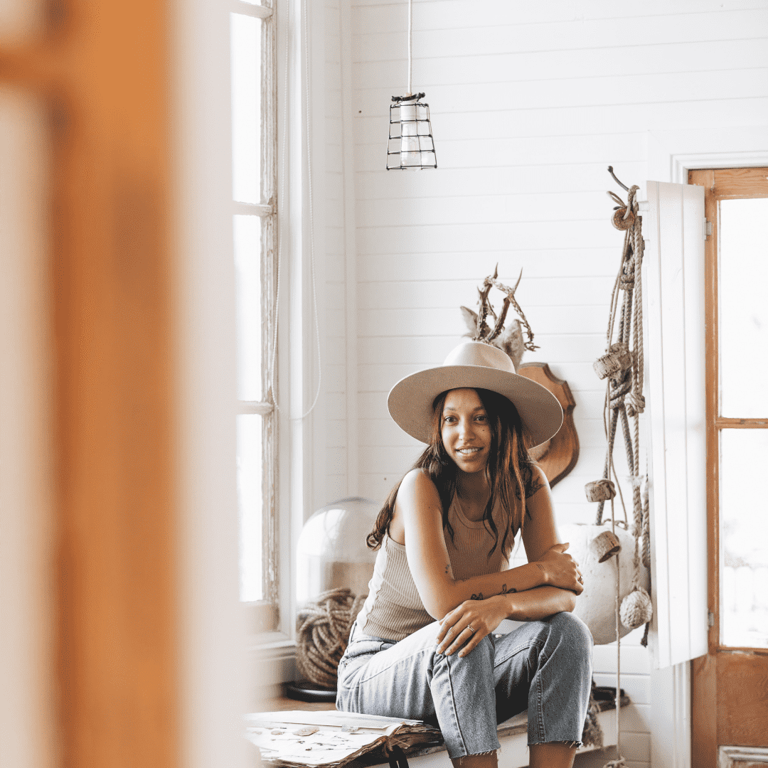 Woman wearing a wide brim wool hat sitting inside a cabin at Captains Rest