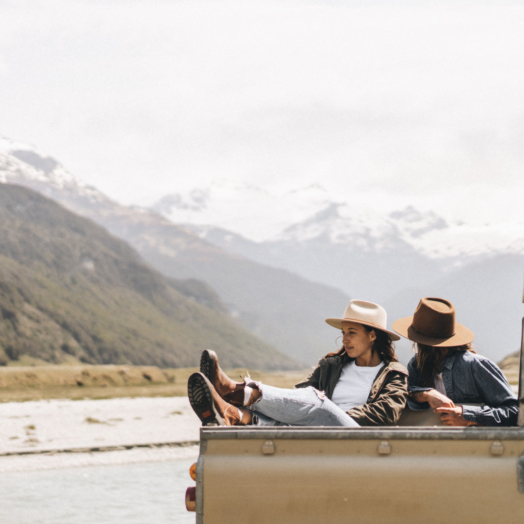 Two women sit in the back of a Land Rover tray looking at the view of the surrounding mountains