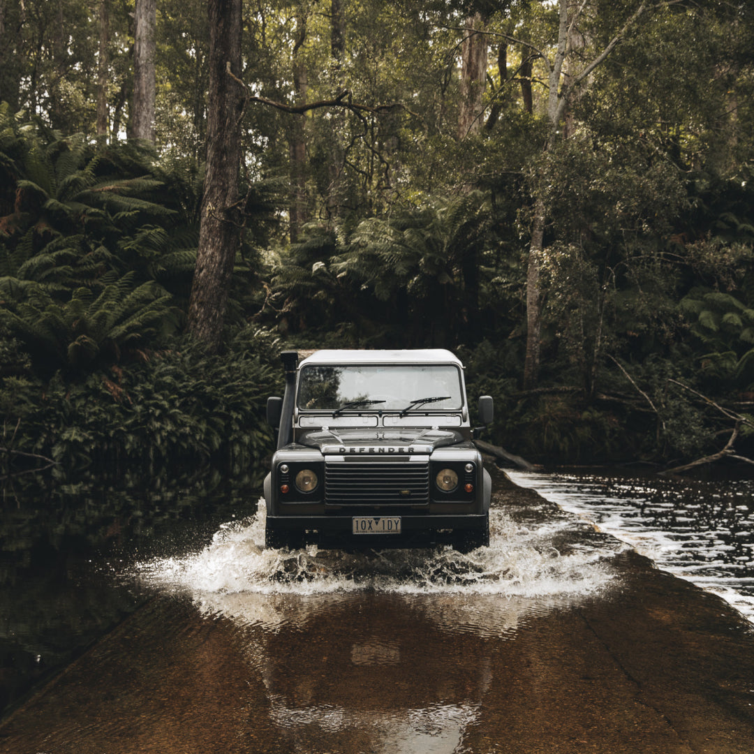 A Land Rover driving through water in the forest in Tasmania