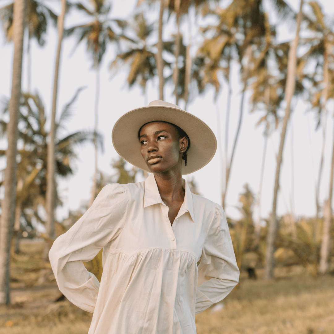 A woman wearing a wide brim wool hat standing in front of palm trees
