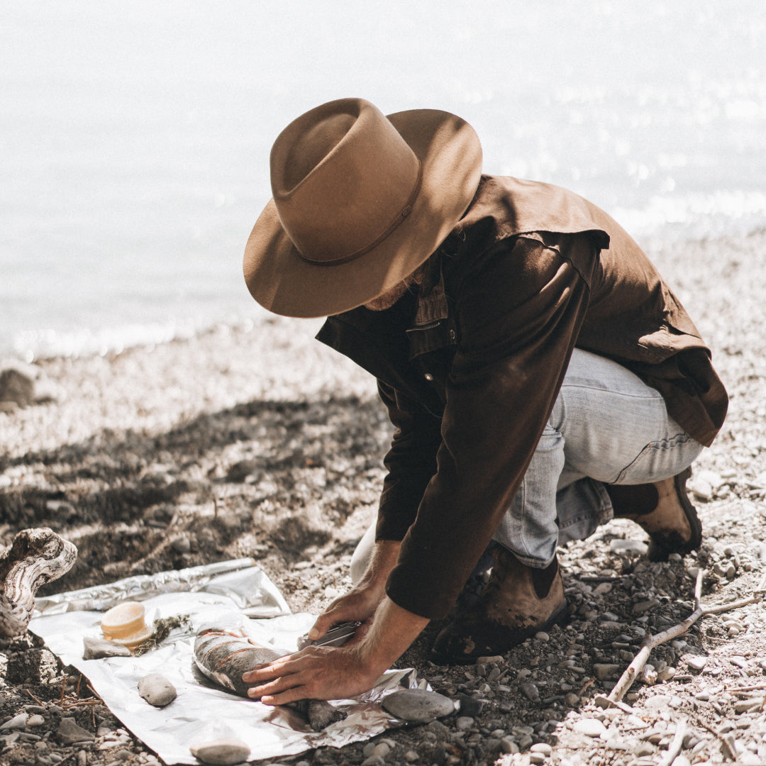 A man is preparing a freshly caught fish on the ground ready to be cooked