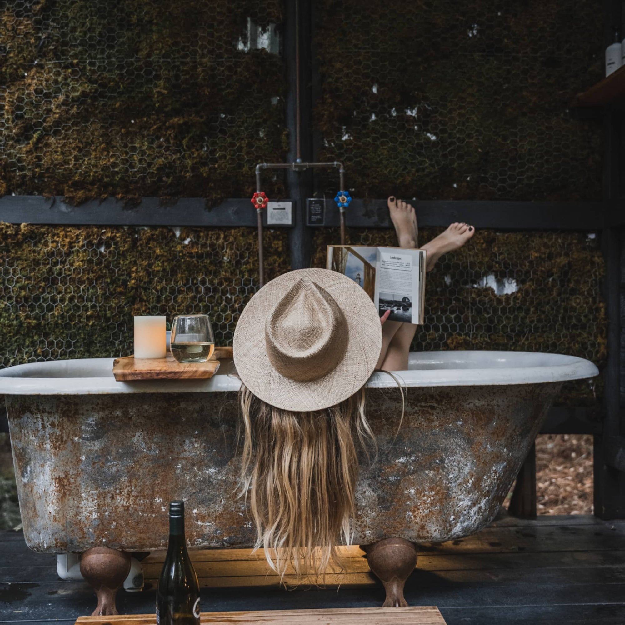 Melissa sitting in an outdoor bath with a book and a wine