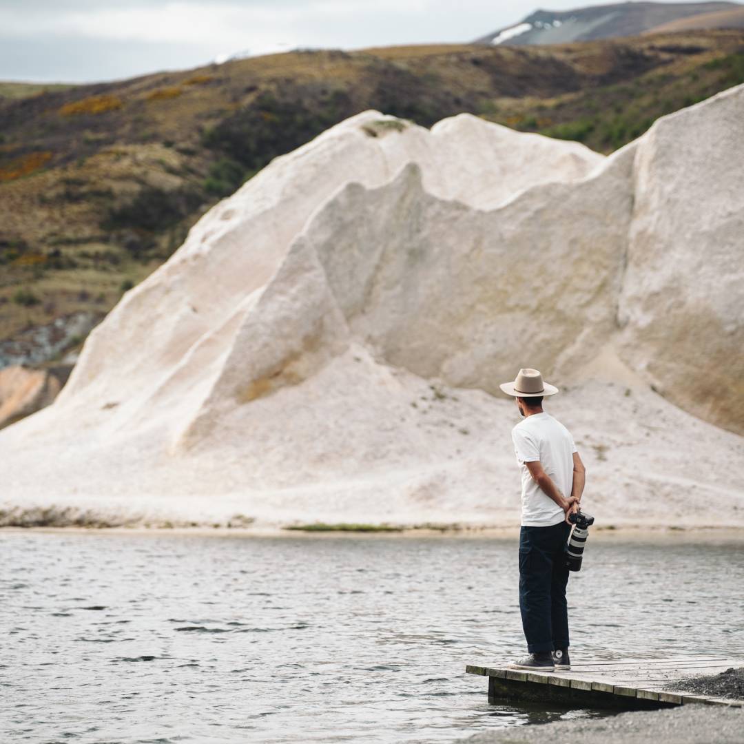 Marc standing on a jetty looking out over the water with rock formations in the background