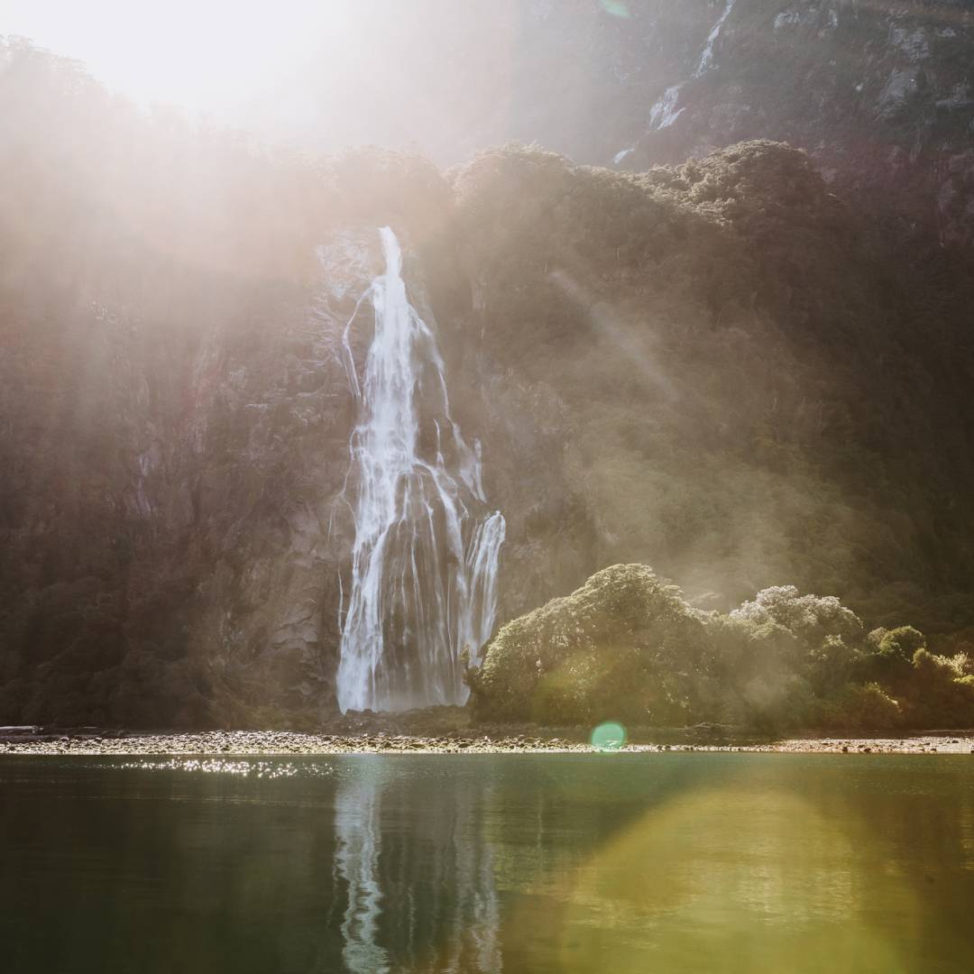 Sunlight spilling over the top of a water fall across the other side of a lake