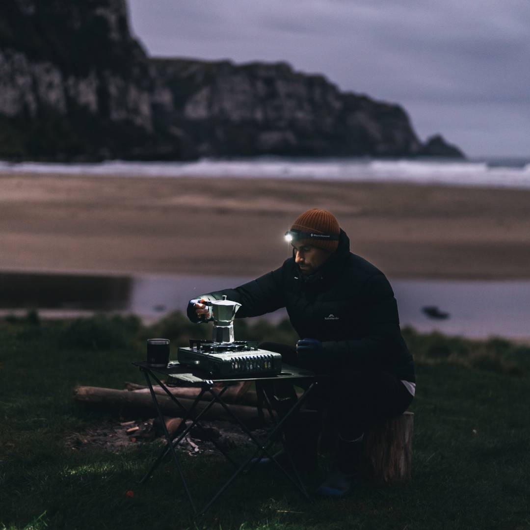 Marc preparing a camp coffee at dusk under the light of his head torch