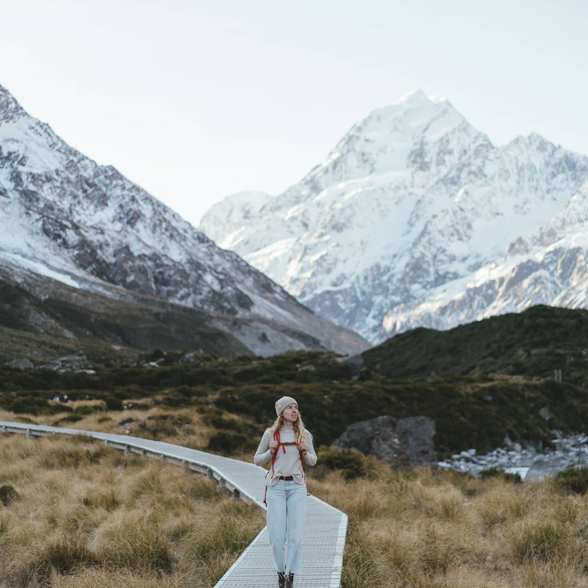 A woman hiking on a boardwalk through the Hooker Valley in New Zealand