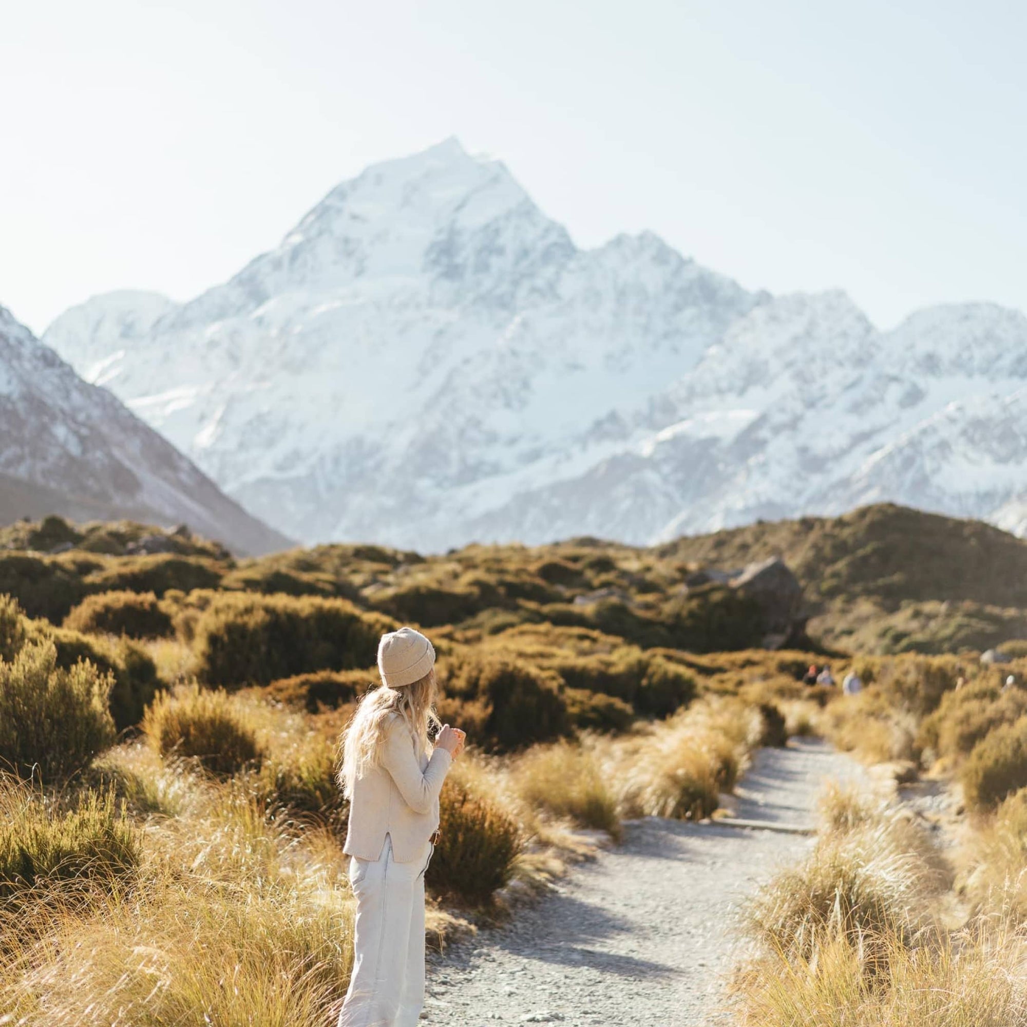 A woman standing on a gravel trail in the middle of a New Zealand valley
