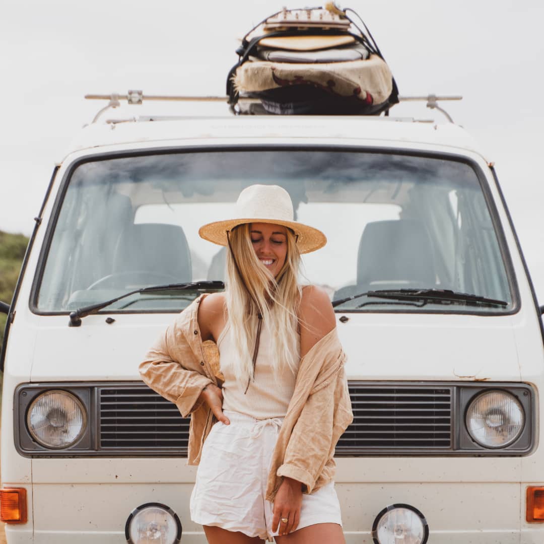 Kendall standing in front of her can wearing a white linen outfit with a wide brim straw hat