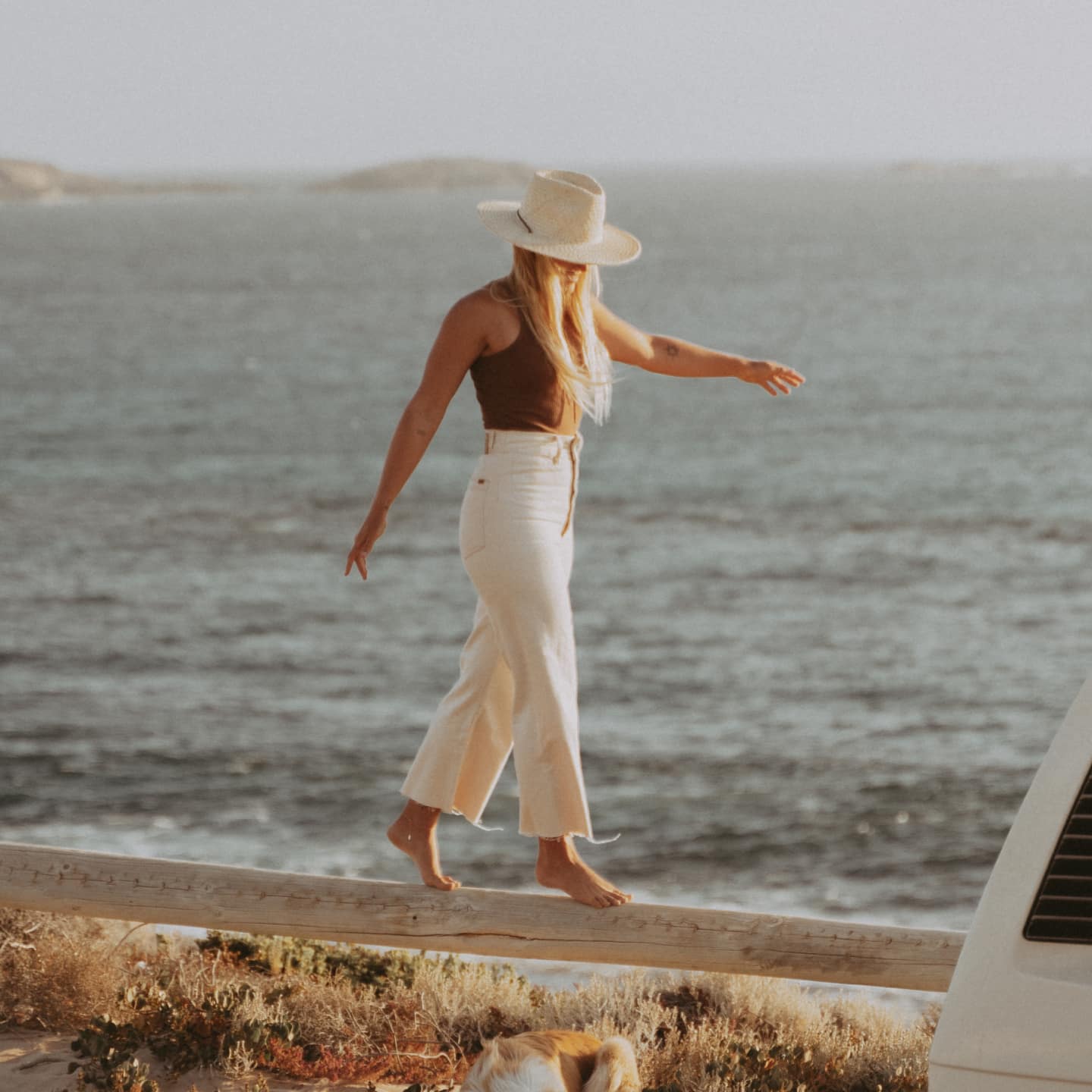 Kendall walking across a wooden beam with the ocean in the background