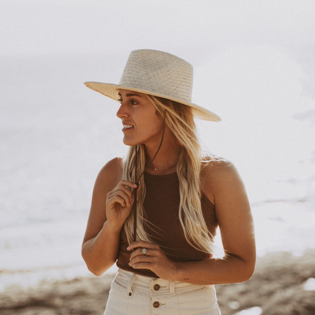 Woman with long blonde hair wearing a wide brim straw hat, tightening the hat lanyard