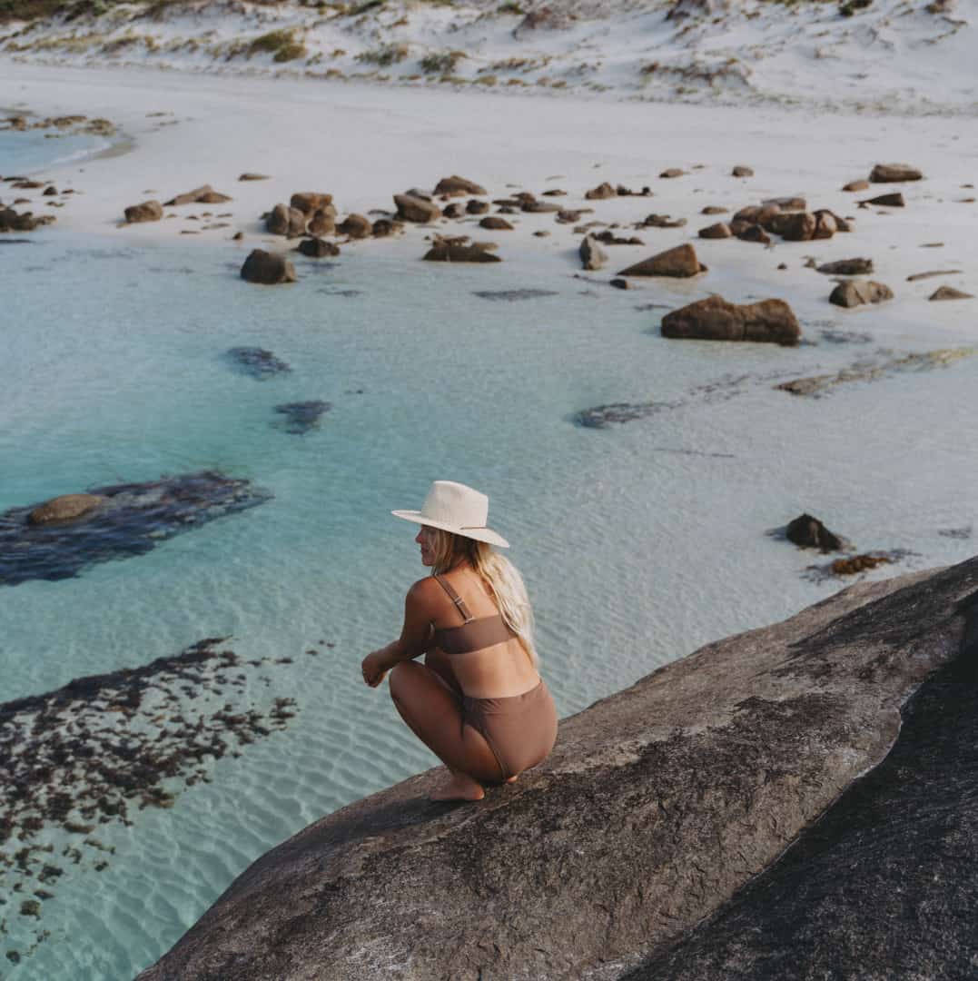 Kendall squatting on top of a rock next to the ocean