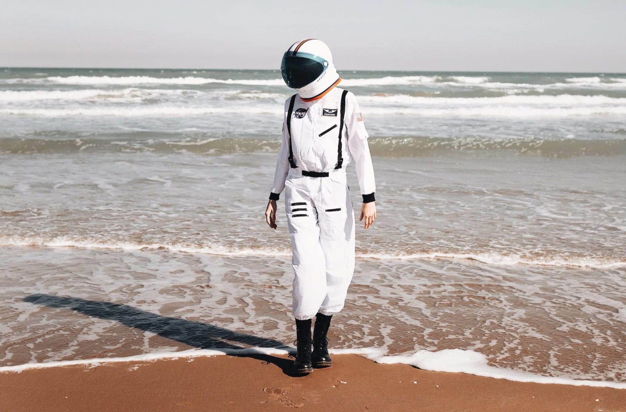 Person dressed in an astronaut suit walking across the beach shore