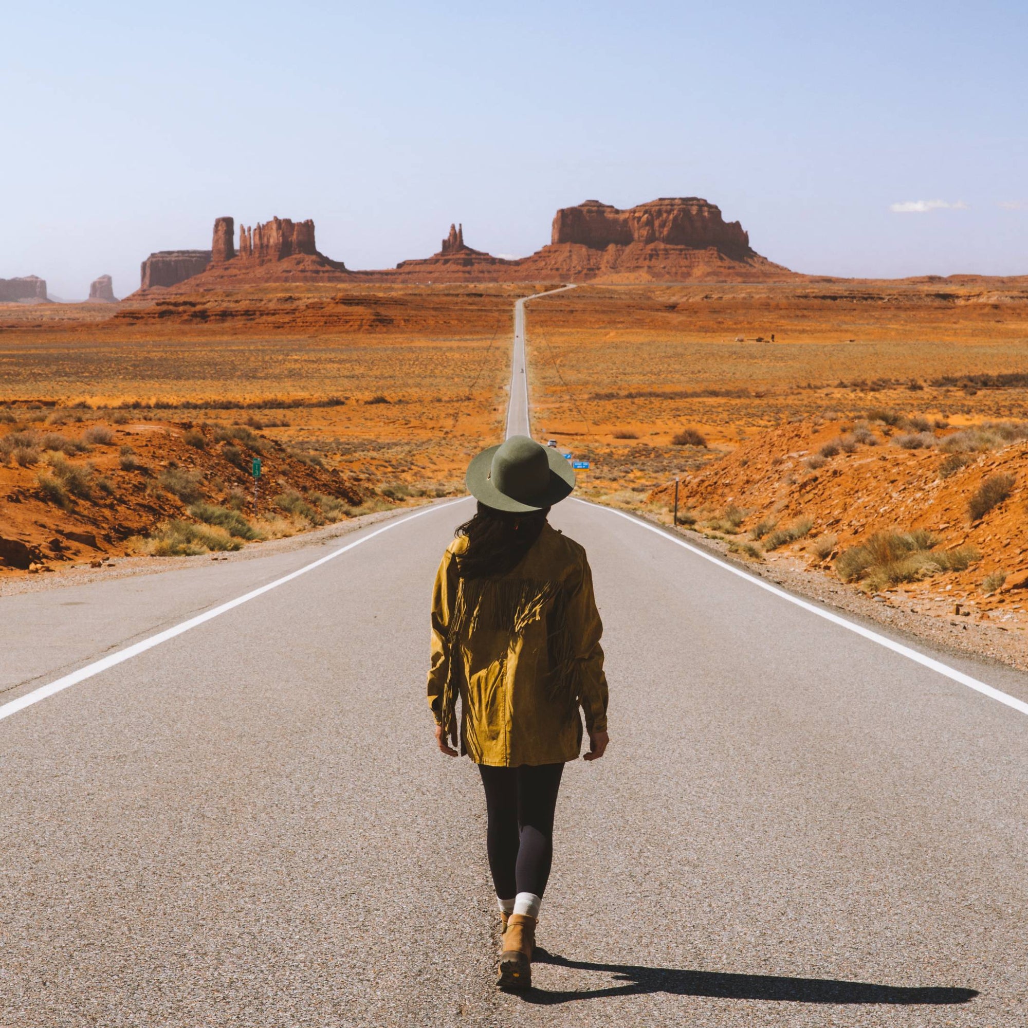 Blanca stands in the middle of a long desert road looking at the mountains in the distance
