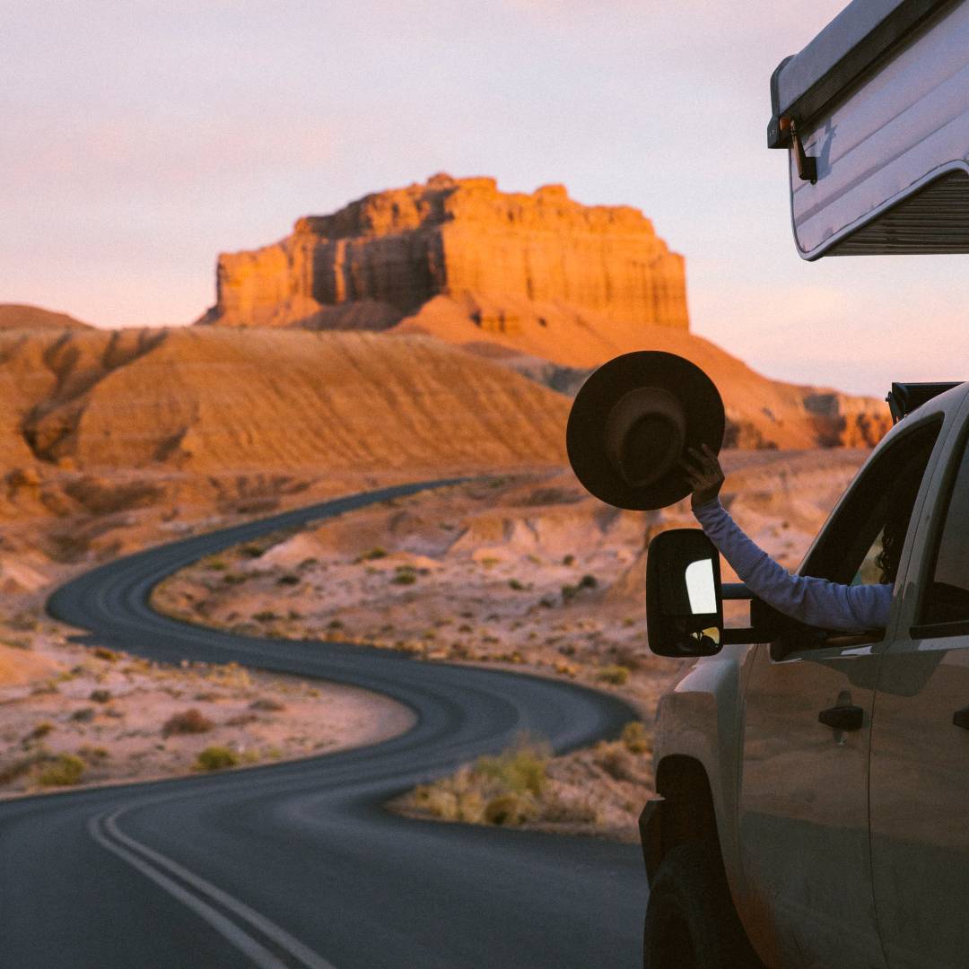 A person holds a wide brim wool hat out the window while driving down a long winding road in the middle of the Utah desert