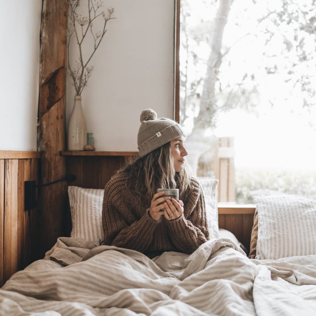 Woman sitting under the blankets on a bed holding a hot cup of tea