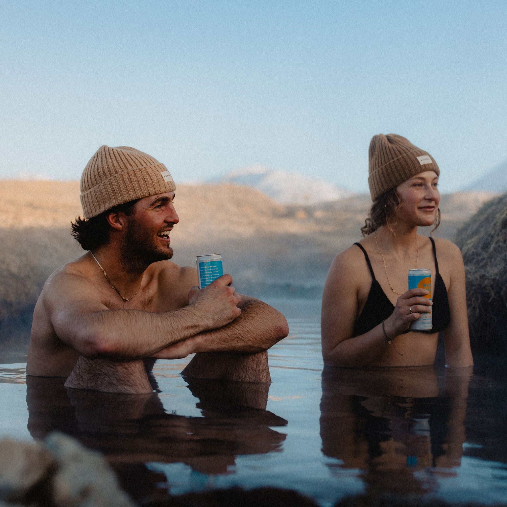 Man and a woman wearing beanies and sitting in a hot spring