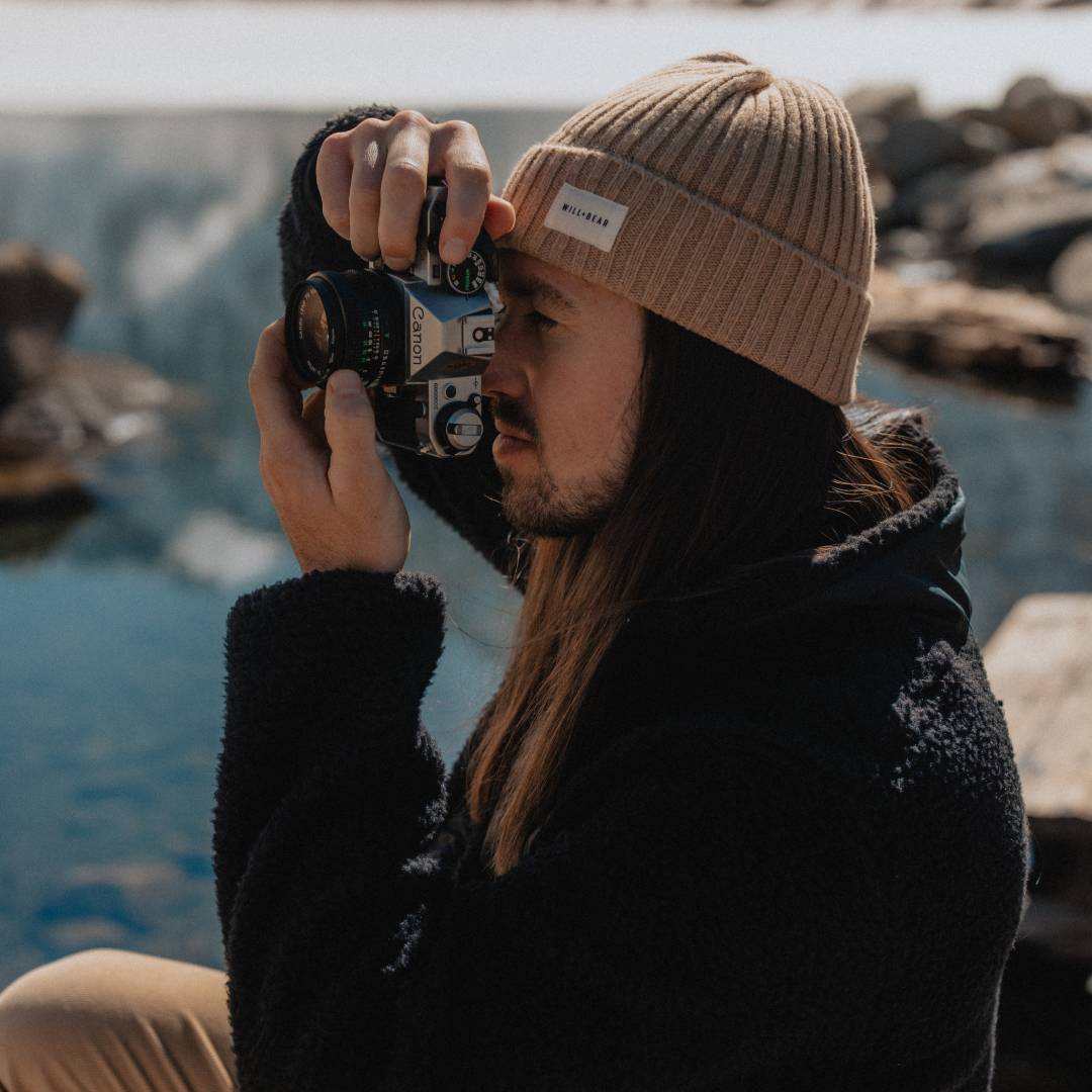 Man with long hair wearing a beanie and taking a photo outdoors