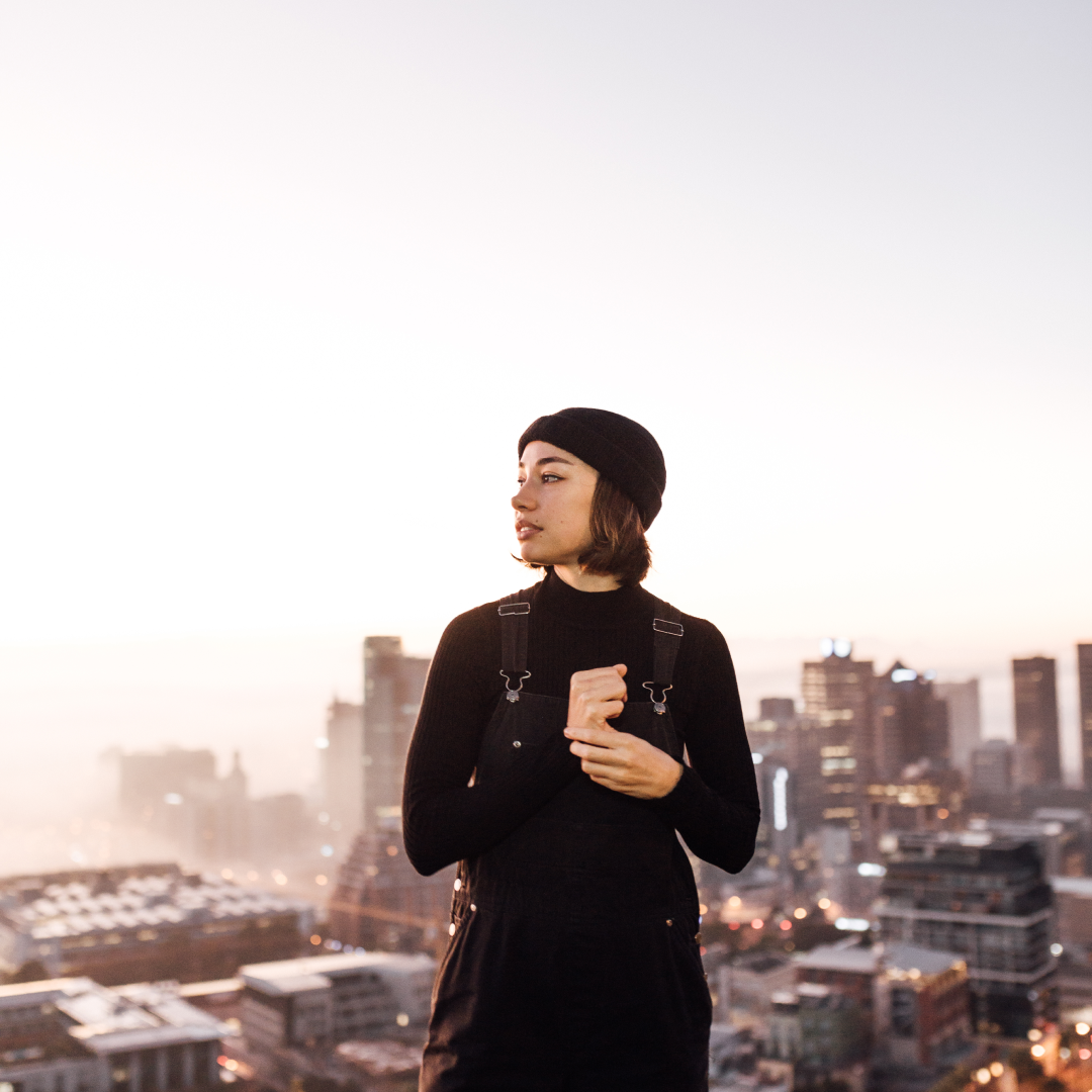 A close up photo of a women wearing a beanie with the city scape behind her